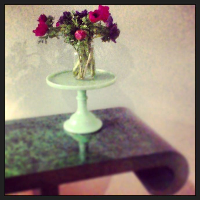 Nomad Luxuries showcasing antiqued green table with flowers for a pop of color. 