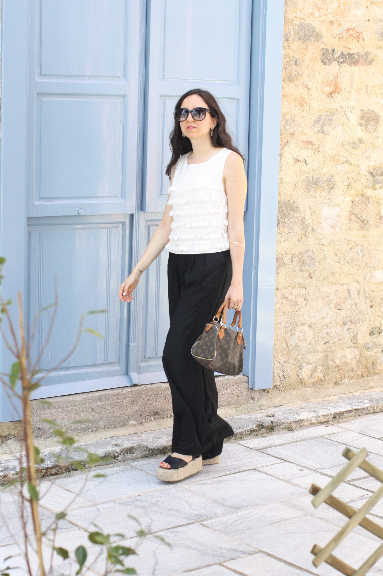 Yana Puaca of NoMad Luxuries wearing a white tassel top and black palazzo pants with asos flatform shoes and a louis vuitton purse