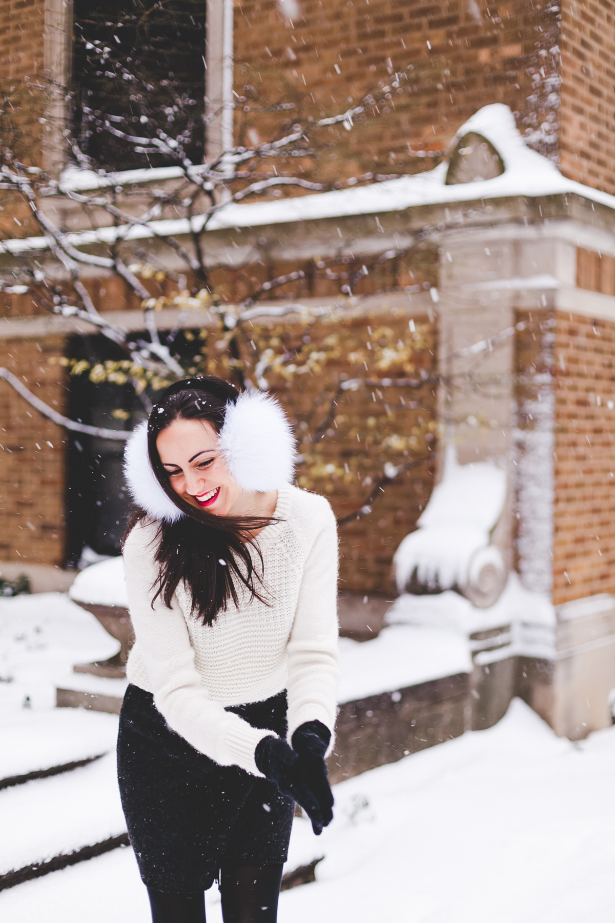 Yana Frigelis of NoMad Luxuries wearing fur earmuffs and a cozy cableknit sweater in the snow for the holidays 