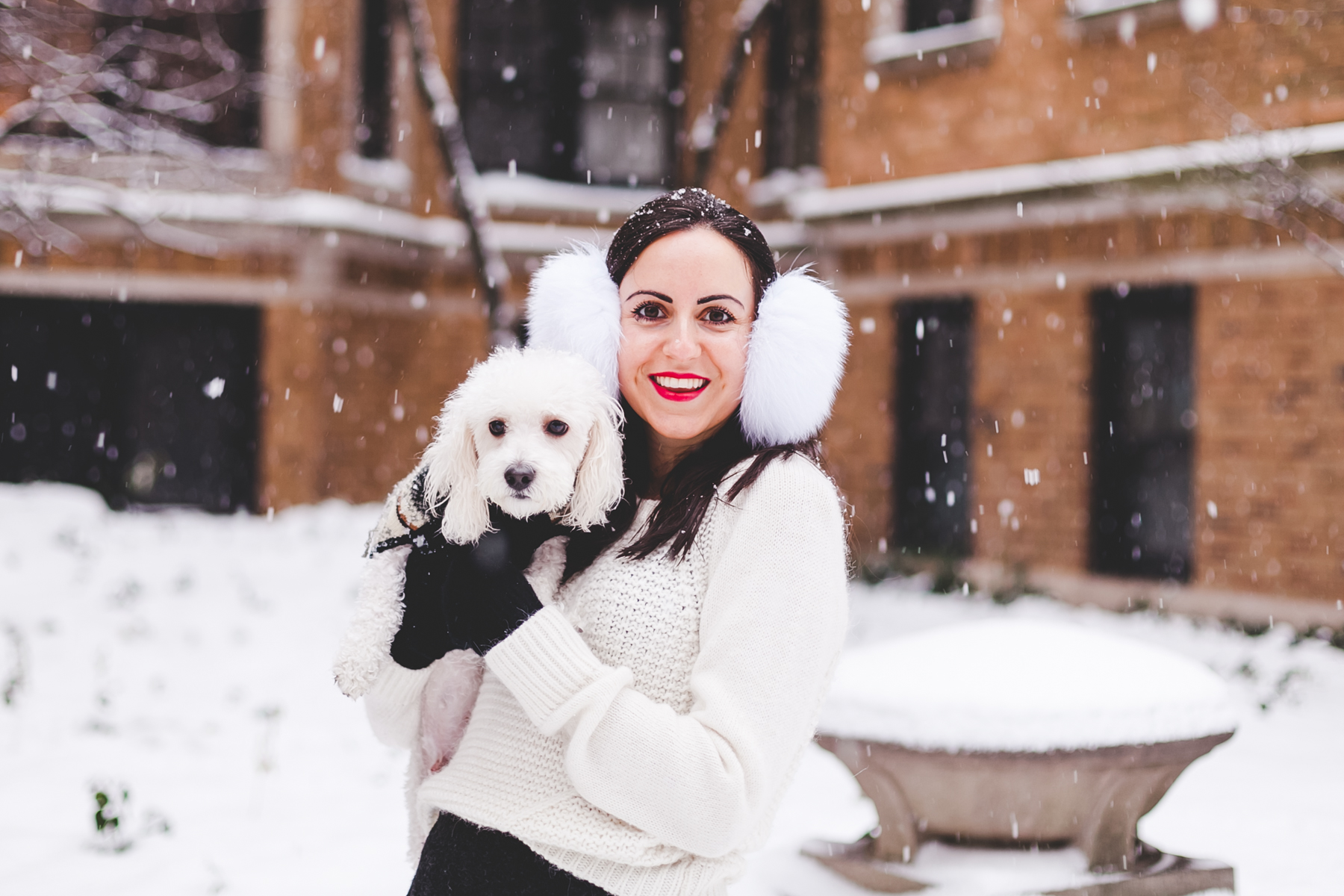 Yana Frigelis of NoMad Luxuries wearing fur earmuffs and a cozy cableknit sweater in the snow for the holidays 