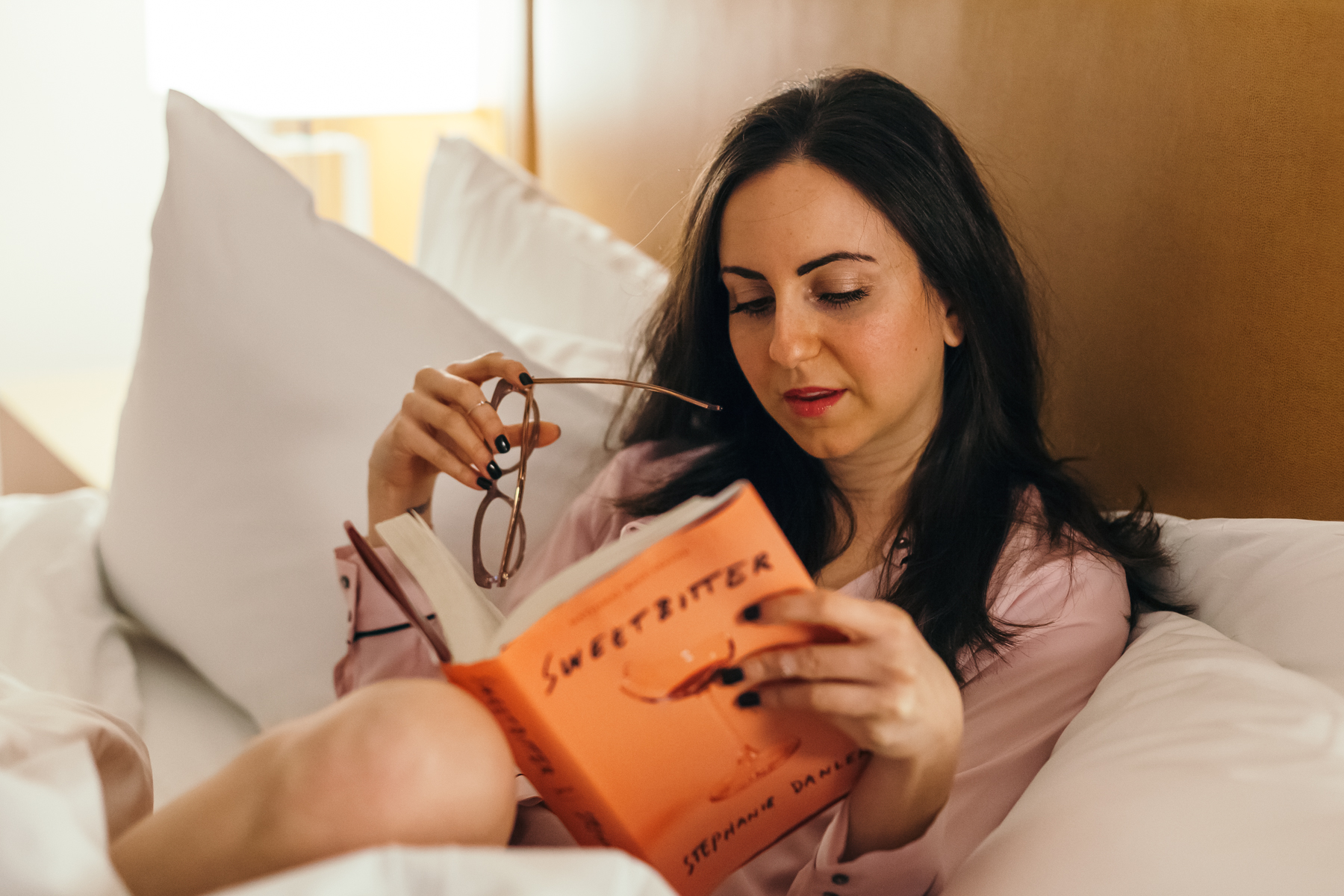 Yana Frigelis of NoMad Luxuries wearing a mango pink silk pajama blouse in bed