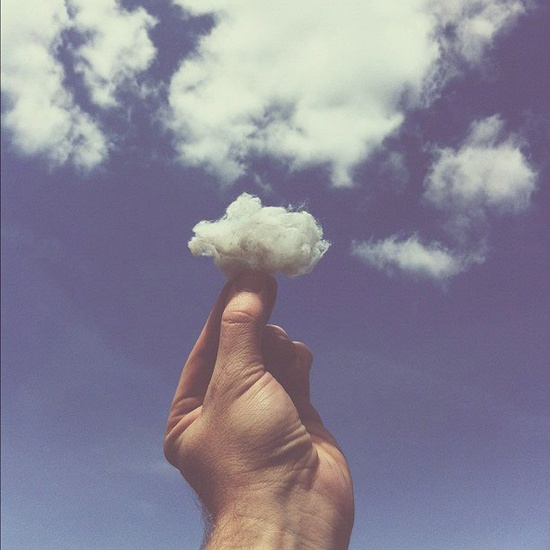 A whimsical photo of someone holding up a cotton ball to emulate the clouds in the sky. 