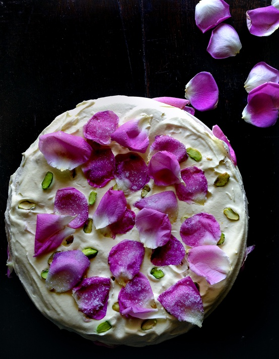 Nomad Luxuries; flat lay photo of a hand frosted pistachio cake with rose petals for a finishing touch. 
